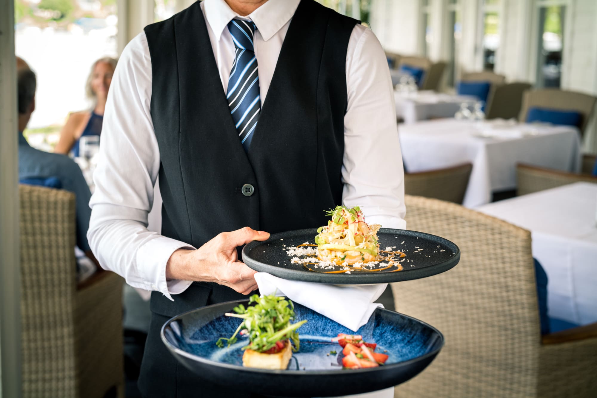 Serveur apportant des assiettes gastronomique dans la salle du restaurant Le Riverain