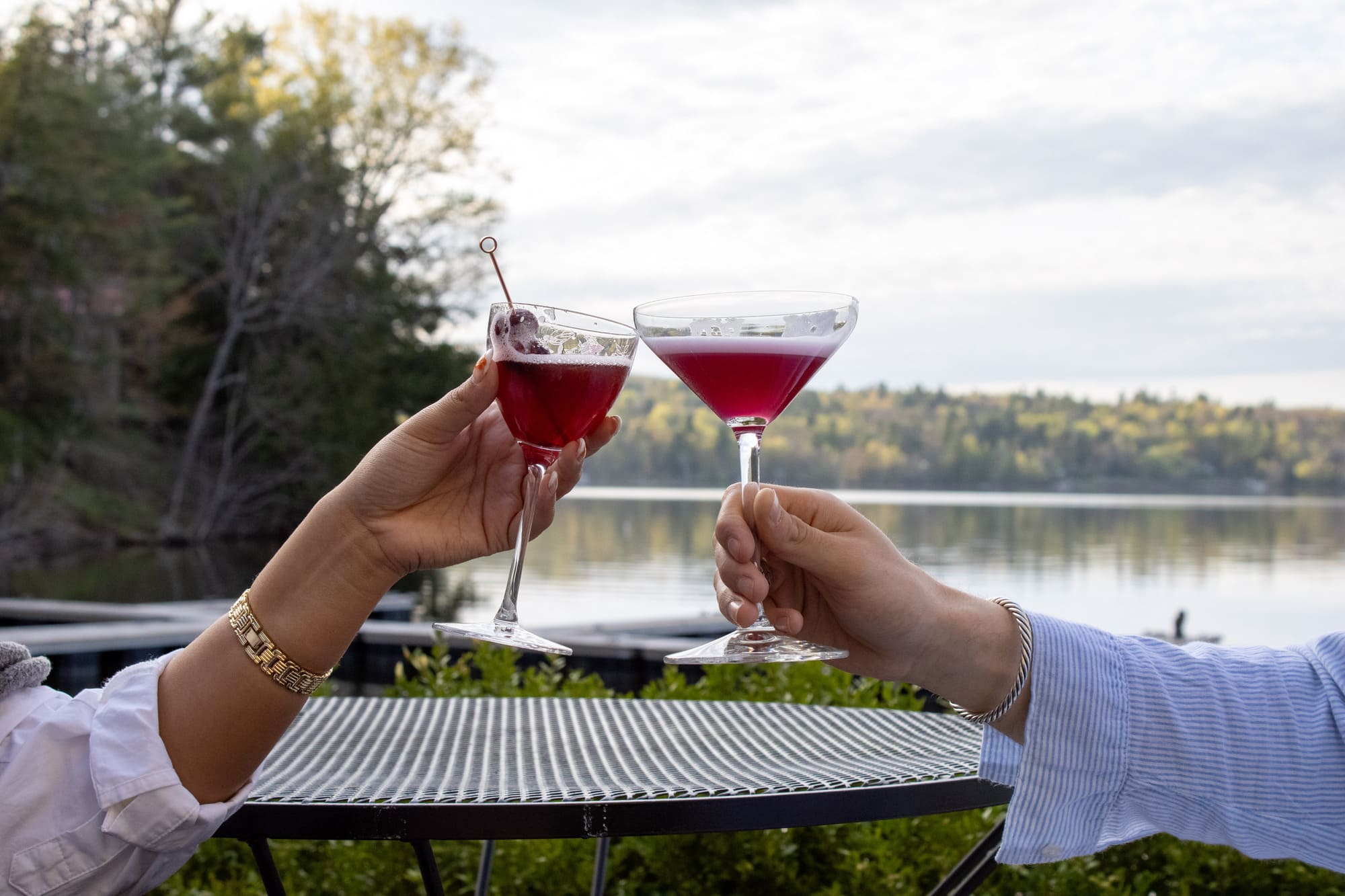 Deux personnes trinquent avec des cocktails en terrasse face au lac au restaurant Le Riverain