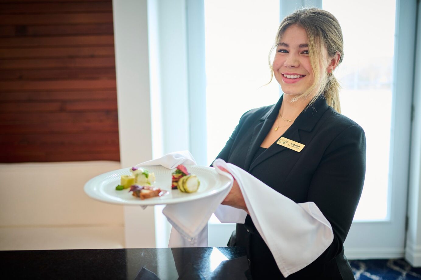Serveuse souriante présentant une assiette gastronomique au restaurant Le Riverain