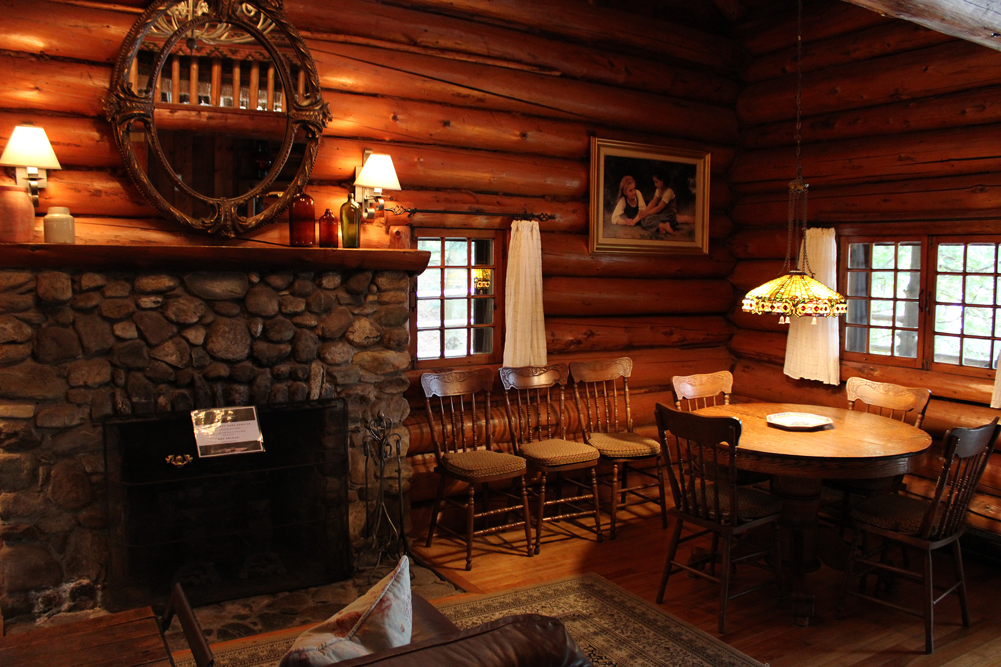 Intérieur chaleureux d’un chalet en bois rond avec foyer en pierre et salle à manger en Estrie